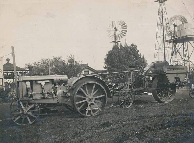 Side view of a tractor coupled to a harvester in front of 2 windmills.