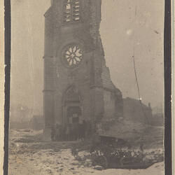Ruins of church with group of people standing by door, broken cart on snowy ground in foreground.