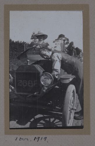 Man leaning over a car hood, with two people seated in car.