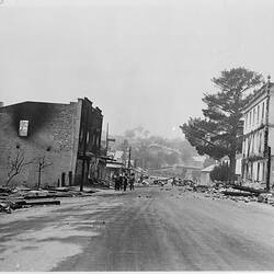 Fire damaged buildings either side of a street. Group of men stand in the distance.