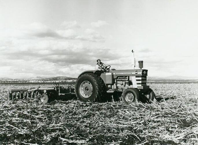 Man driving a tractor coupled to a plough across a stublble field.
