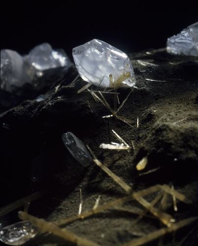 Pale blue-white flatish crystals surrounded by sparse elongated yellow crystals.