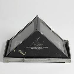 Triangular glass roofed container with black hinged metal frame on base. Text printed on black metal side.