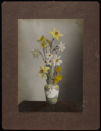 Still life of yellow and white daffodil flowers in an ornate vase.