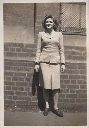 Woman in skirt suit standing against brick wall.