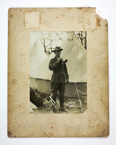 Soldier with trumpet in hand next to tent.