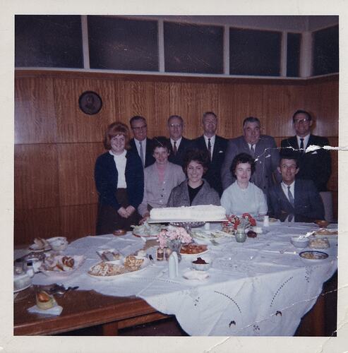 Group seated behind food and cake on table.