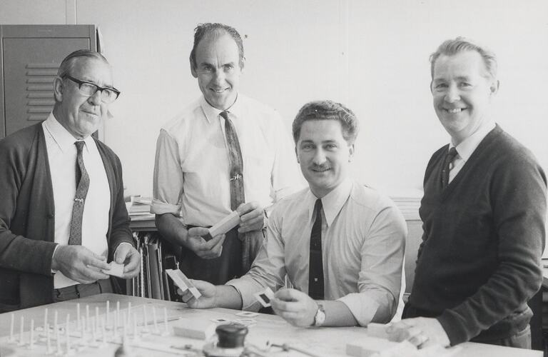 Four men looking at slides on table.