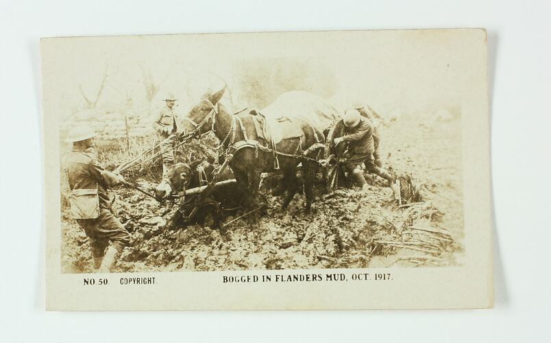 Soldiers pulling two horses and a wagon that are bogged in the mud.