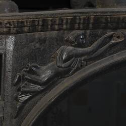 Black wooden hearse, detail of decorative woodwork. Female figure, arms extended.