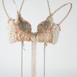 Cream pearl brassiere with pink and blue beads. Gold chain neck, shoulder straps. Back.