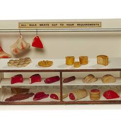 Butcher shop model with meat displays above and on countertop.
