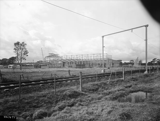 Multi-storey building under construction with a railway line and grass field in the foreground.