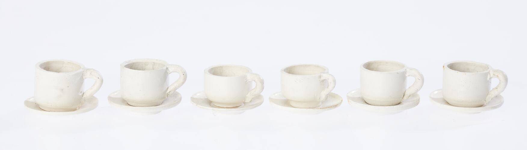 Model of six miniature white cups and saucers.