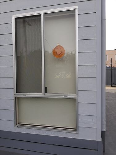 Crocheted yellow smiling sun hanging in window of grey weatherboard house.