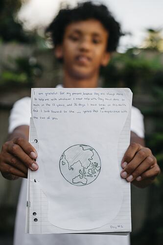 Boy holding up sheet with drawn picture of the world.