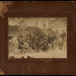 Group of construction workers pose on rocky worksite with machinery behind them.