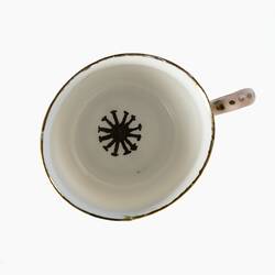 White tea cup from above. Inside base has sun motif in gold paint. Gold painted handle.