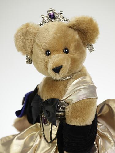 Light brown plush bear in black velvet and gold lame gown. Faux diamond, amethyst tiara, necklace, earrings.