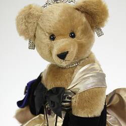 Light brown plush bear in black velvet and gold lame gown. Faux diamond, amethyst tiara, necklace, earrings.