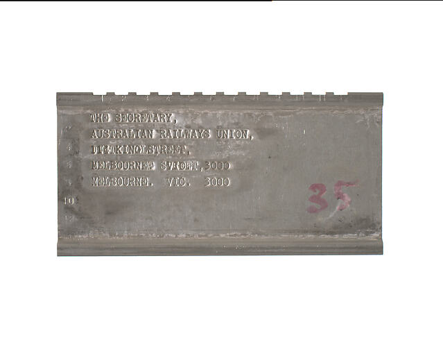 A shiny silver-colour, metal plate with embossed text giving details of addressee.