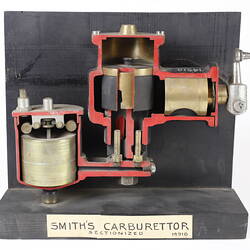 Sectioned Smith's carburettor on black stand with label.