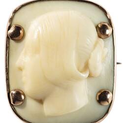 Square cameo with rounded corners featuring a white female bust facing left, hair up in a bun. Four prominent corner gold pins secure the cameo to its gold setting.