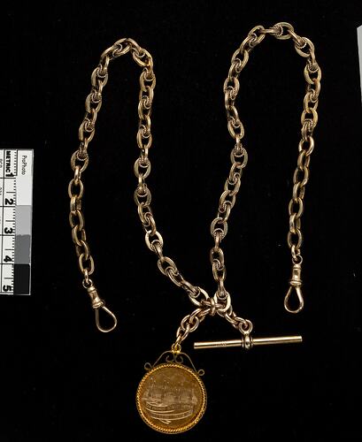 Front of gold round fob with chain and T-bar.