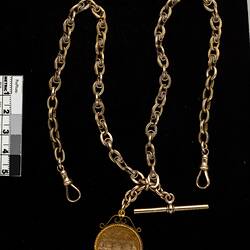 Front of gold round fob with chain and T-bar.