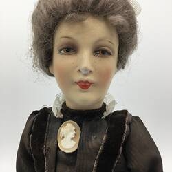 A doll dressed in a dark brown dress with a cameo brooch
