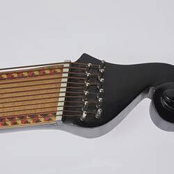 Detail of timber stringed instrument. Pale wood neck with zig zag pattern on edges. Stylised curved black laquered head stock. 61 strings in varied thickness.