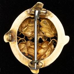 Back of round gold brooch with vertical pin.