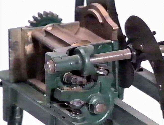 Detail of chaffcutter model made from metal featuring large rotating wheel with two blades controlled by rotating handle.