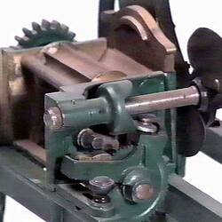 Detail of chaffcutter model made from metal featuring large rotating wheel with two blades controlled by rotating handle.