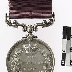 Silver coloured medal With crown in top-centre, text below, surrounded by wreath, with maroon ribbon.