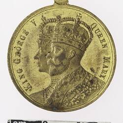 Round gold coloured medal with profile of a man and woman with crowns, text surrounding.