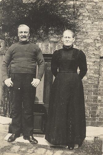 Man and woman in dark clothes standing in front of brick building.