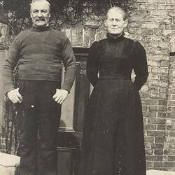 Man and woman in dark clothes standing in front of brick building.
