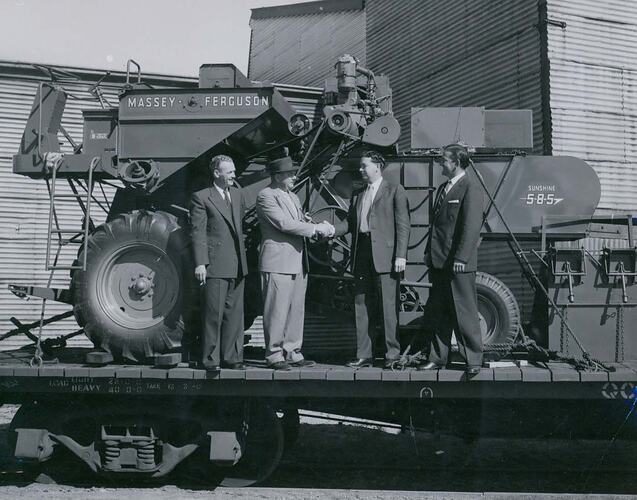 4 men standing on rail wagon in front of harvester.