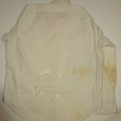 Back view of men's, off-white long sleeve shirt. Has tears and brown stains on lower section and right elbow.
