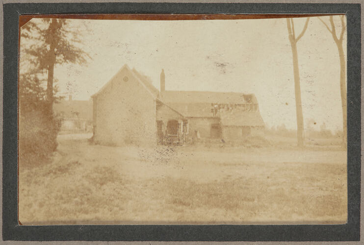 A damaged farm house building, with trees and shrubs located around the house.