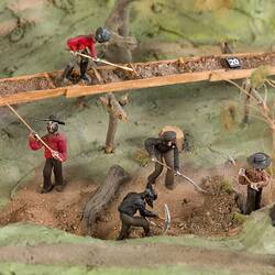 Mining display model, detail. Mining figures using tools on rough green ground.