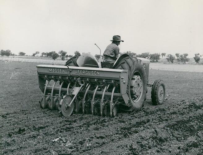 A man driving a tractor, with a sod seeder attached, across field.