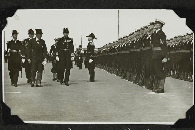 Five men walking past rows of servicemen standing in formation.