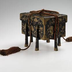 Lidded decorated, four-legged box with tassled ties.