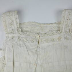 The top of a white pinafore with crocheted detailing.