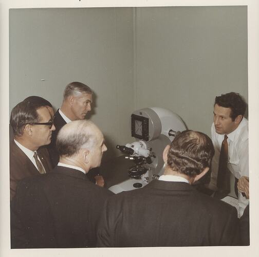 Five men around microscope on a table.
