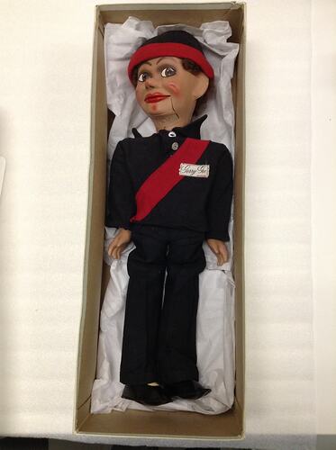 Doll wearing black sport uniform with red diagnola stripe on jumper. Housed in box.