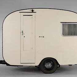 Cream caravan, curved edges. One side window and door. Two wheels and tow bar.