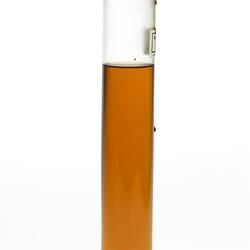 Cylindrical glass jar with amber coloured liquid. One label affixed, sealed at top.
